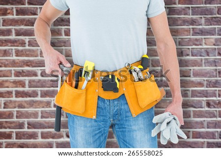 Technician holding gloves and hammer against red brick wall
