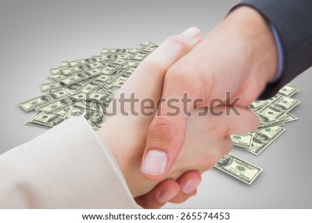 Close up on new partners shaking hands against pile of dollars