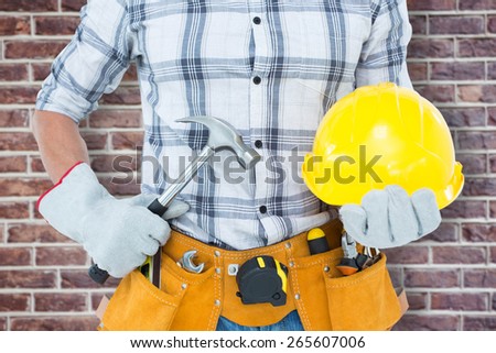 Handyman holding hammer and hard hat against red brick wall