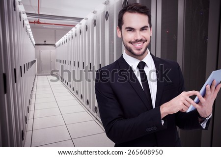 Businessman using his tablet while looking at the camera against data center