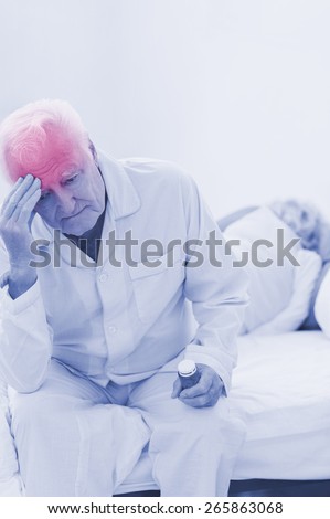 Old man having a headache while woman sleeping on the bed