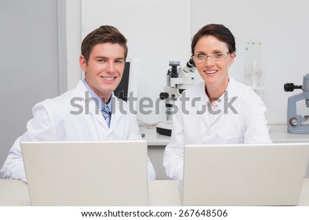 Scientists working with laptop and smiling at camera in laboratory