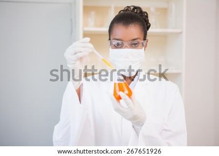 Concentrated scientist examining orange fluid with pipette in laboratory