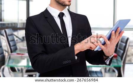 Mid section of a businessman using digital tablet pc against empty corporate meeting room