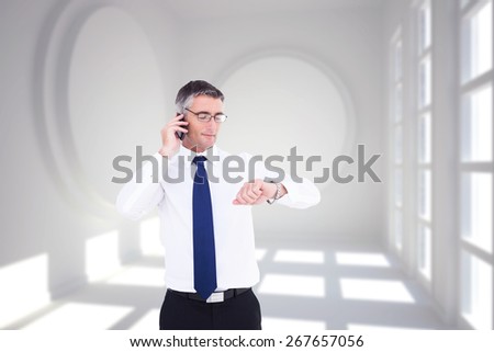 Businessman on the phone looking at his wrist watch against white room with circles at wall