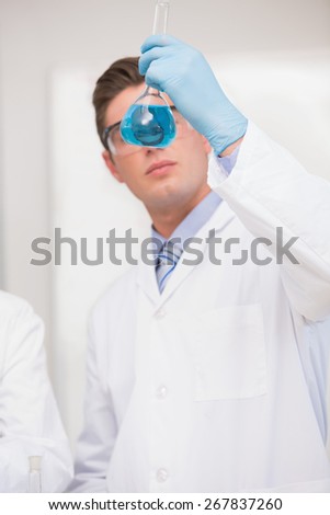 Scientist looking at beaker with blue fluid in laboratory