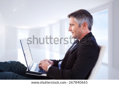 Businessman using laptop against bright white corridor with windows