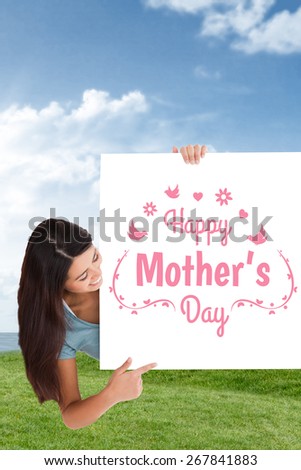 Attractive woman pointing at a board against field and sky