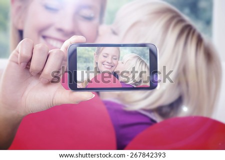 Hand holding smartphone showing against happy mother and daughter on the couch with heart card