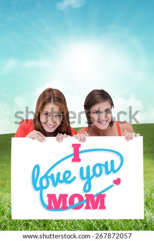 Teenage girls smiling while holding a blank poster and hiding behind it against field and sky