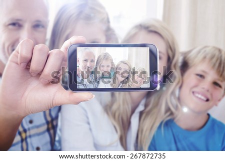 Hand holding smartphone showing against happy family sitting on couch together