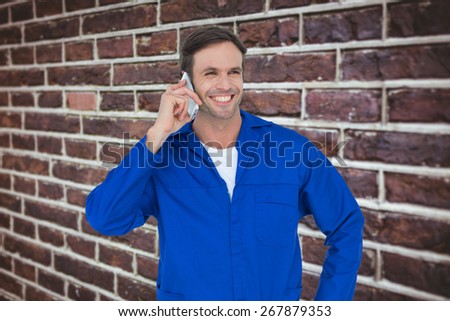 Mechanic using mobile phone over white background against red brick wall