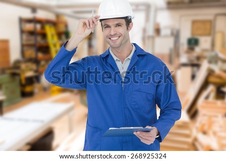 Happy supervisor wearing hard hat while holding clip board against workshop