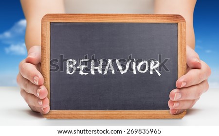 The word behavior and females hands showing black board against bright blue sky with clouds