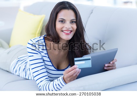 Smiling beautiful brunette doing online shopping on the couch in the living room