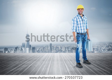 Manual worker with hammer and toolbox against room with large window looking on city