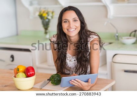 Pretty brunette using tablet pc and preparing salad in the kitchen