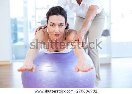 Trainer helping woman on exercise ball in medical office
