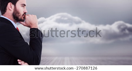 Thinking businessman standing with hand on chin against clouds in a room