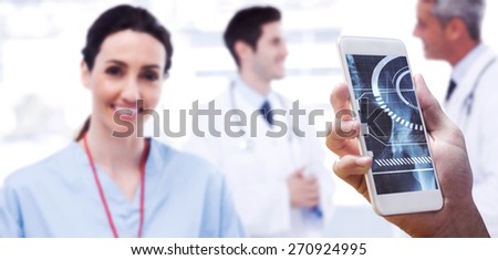 hand holding smartphone against nurse smiling at camera while doctors are talking together