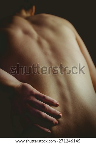 Nude woman with a back injury on black background