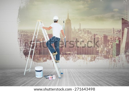 Man on ladder painting with roller against room with large window looking on city