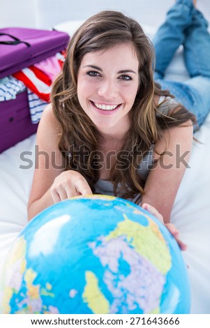Beautiful woman with a suitcase pointing on a globe at home in the bedroom