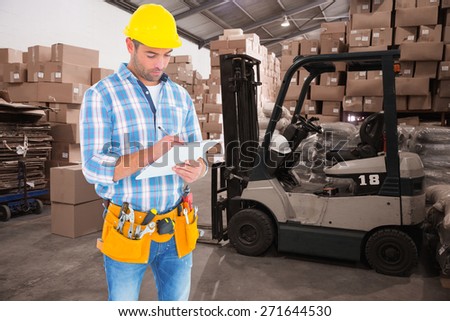 Manual worker writing on clipboard against warehouse worker loading up pallet
