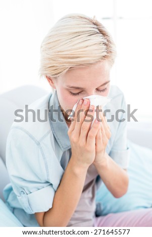 Sick blonde woman blowing her nose in the living room