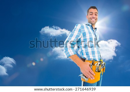 Portrait of smiling handyman wearing tool belt against sky