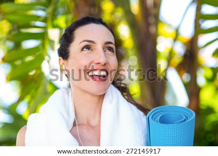 Fit beautiful brunette listening music and holding exercise mat on a sunny day