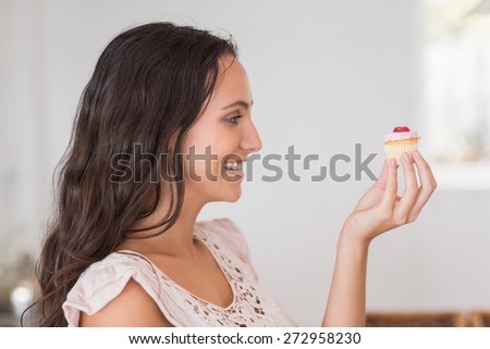 Beautiful brunette holding mini cupcake in the kitchen