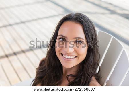 Pretty brunette sitting on a chair and smiling at camera in patio