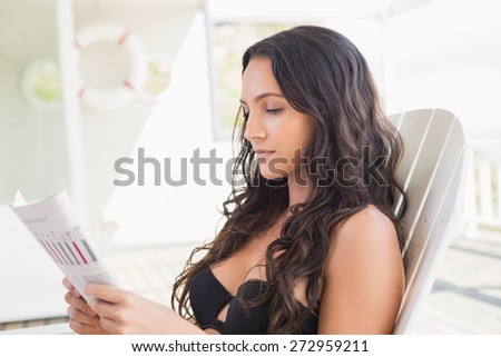Pretty brunette sitting on a chair and reading magazine in patio