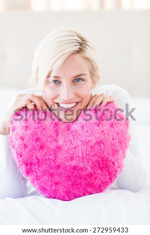 Smiling blonde woman holding heart pillow in the bedroom