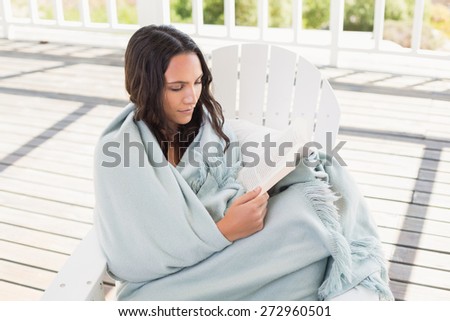 Pretty brunette sitting on a chair and reading a book in patio