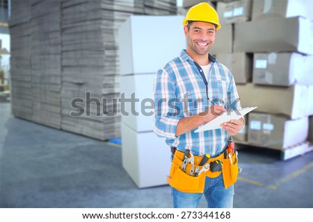 Portrait of smiling handyman writing on clipboard against cardboard boxes in warehouse