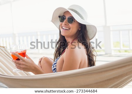 Pretty brunette relaxing on a hammock and drinking cocktail in patio