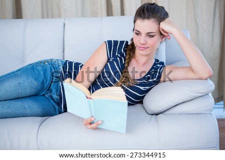 Concentrated woman reading a book on couch at home in the living room