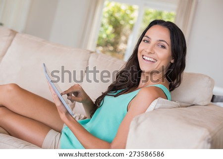 Pretty brunette using her tablet pc at home in the living room