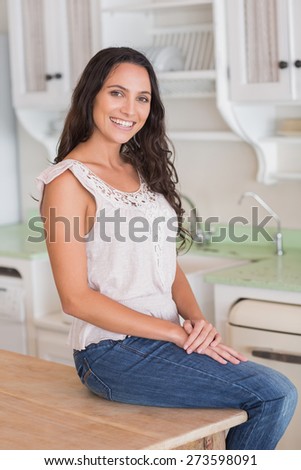 Pretty brunette sitting on table looking at camera in the kitchen