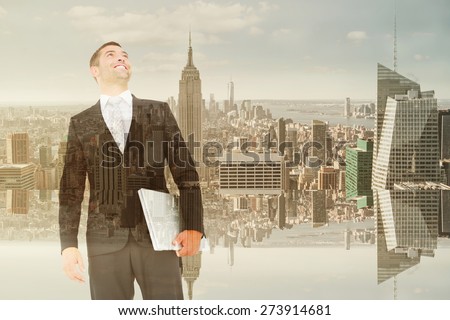 Businessman looking up holding laptop against room with large window looking on city