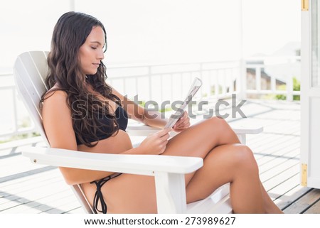 Pretty brunette sitting on a chair and reading magazine in patio