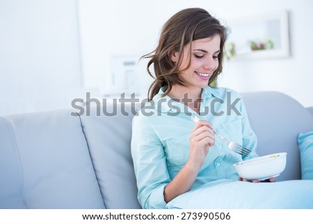 Pretty woman eating bowl of salad at home in the living room