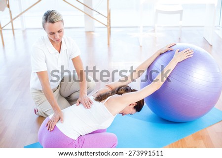 Trainer helping woman with exercise ball in medical office
