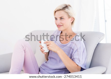 Pretty blonde woman relaxing on the couch and holding a mug in the living room