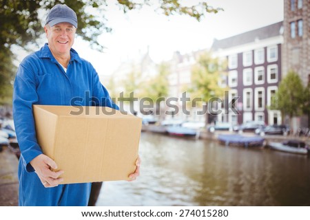 Happy delivery man holding cardboard box against canal in amsterdam