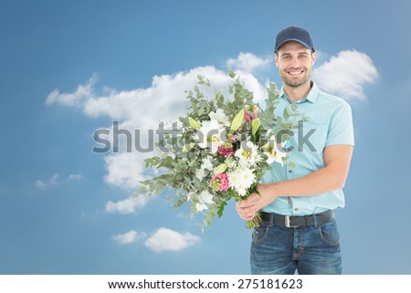Happy delivery man holding bouquet against cloudy sky