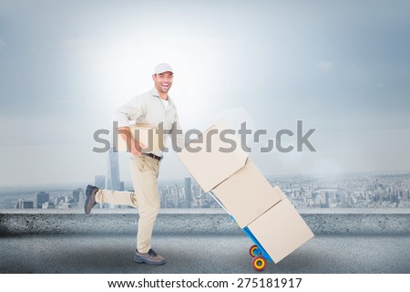 Happy delivery man with trolley of boxes running on white background against cityscape