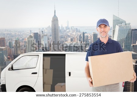 Happy delivery man holding cardboard box against new york